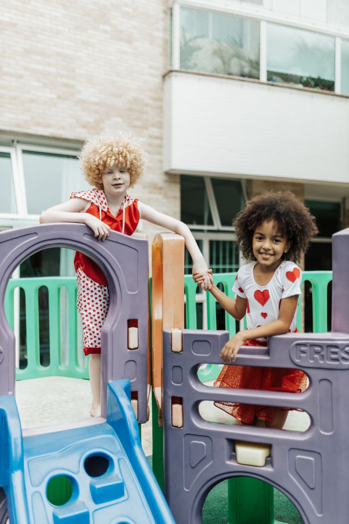 Diverse kids holding hands and smiling while playing on colorful playground equipment.